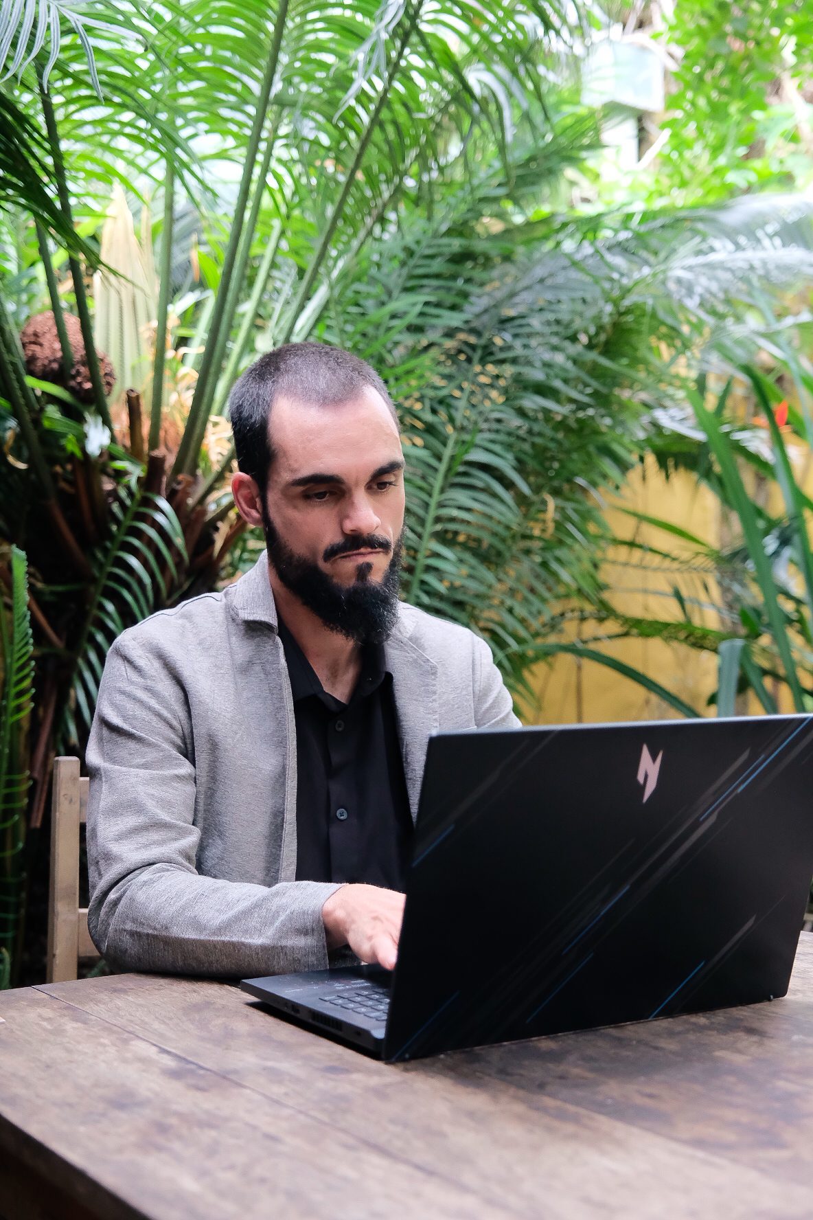Jean Prestes trabalhando no notebook entre palmeiras